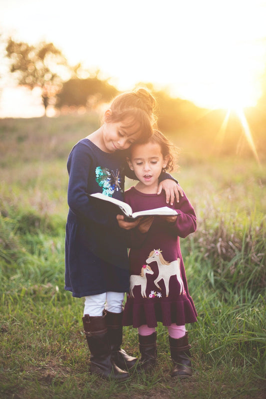 2 girls reading a book outside together