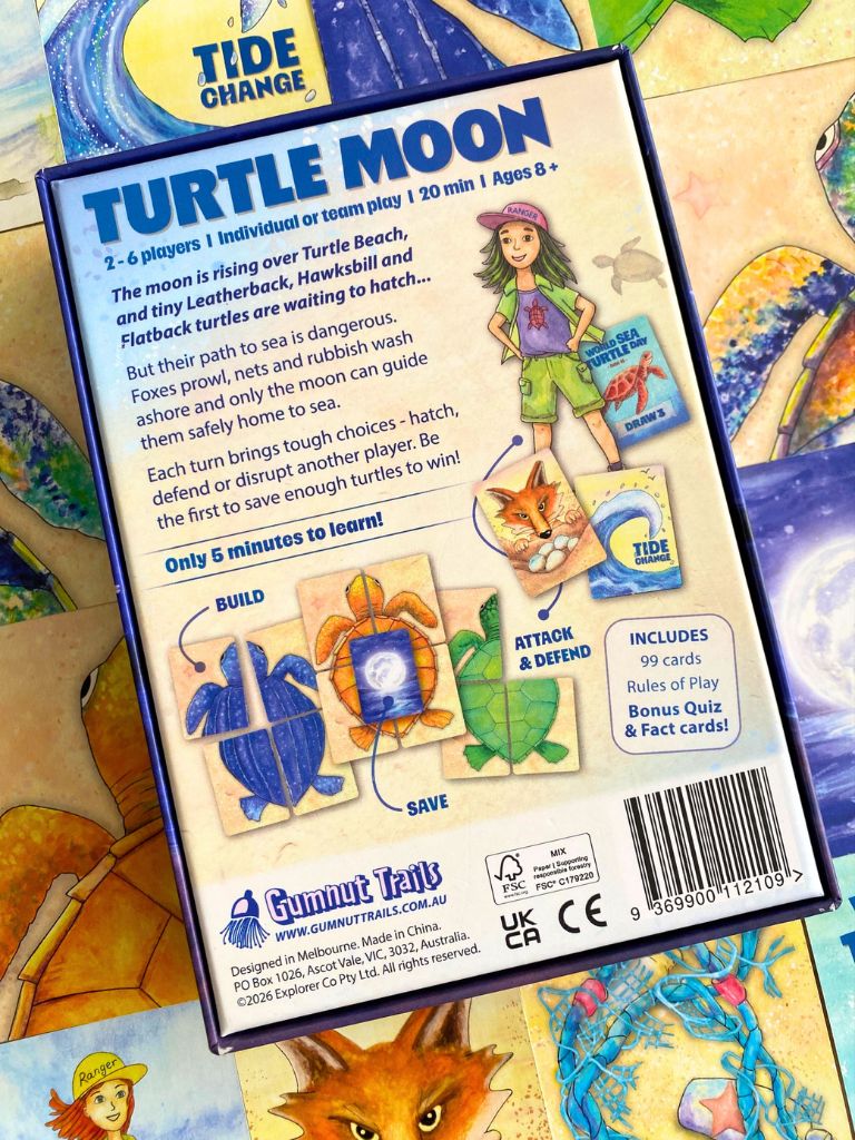 Back of a 'Turtle Moon' card game box by Gumnut Trails, showing rules text, player illustration, and included card counts, photographed over a colorful illustrated game board.