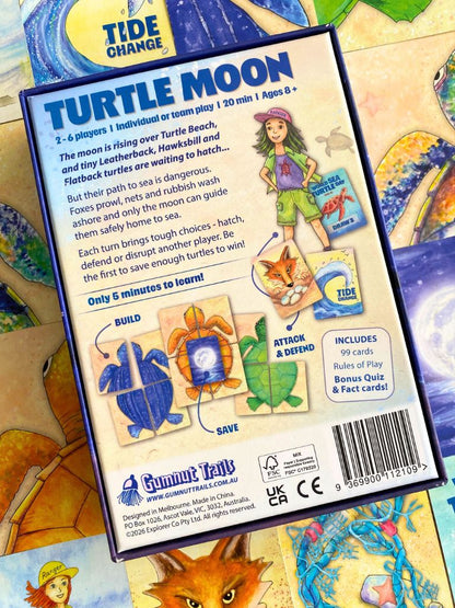 Back of a 'Turtle Moon' card game box by Gumnut Trails, showing rules text, player illustration, and included card counts, photographed over a colorful illustrated game board.