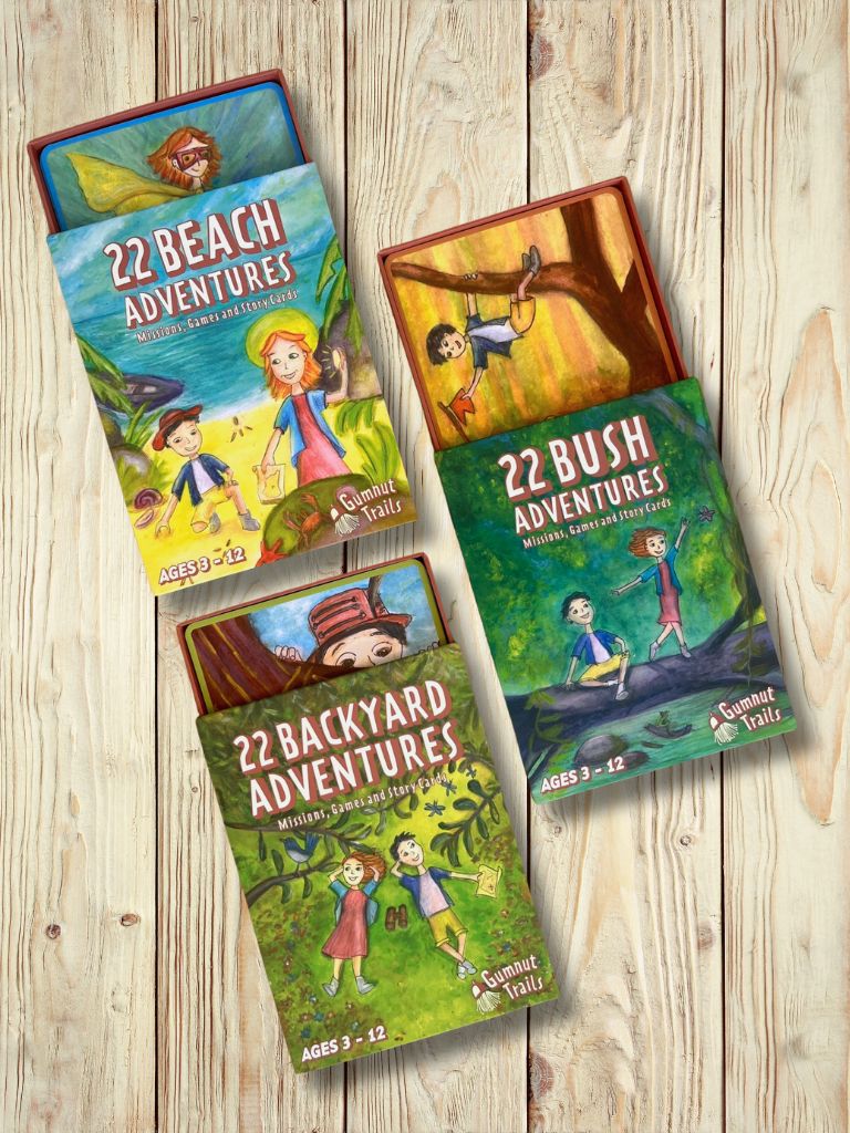 Three children's adventure books on a wooden surface. Gumnut Trails Guides 22 Beach Adventures, 22 Bush Adventures, 22 Backyard Adventures. 