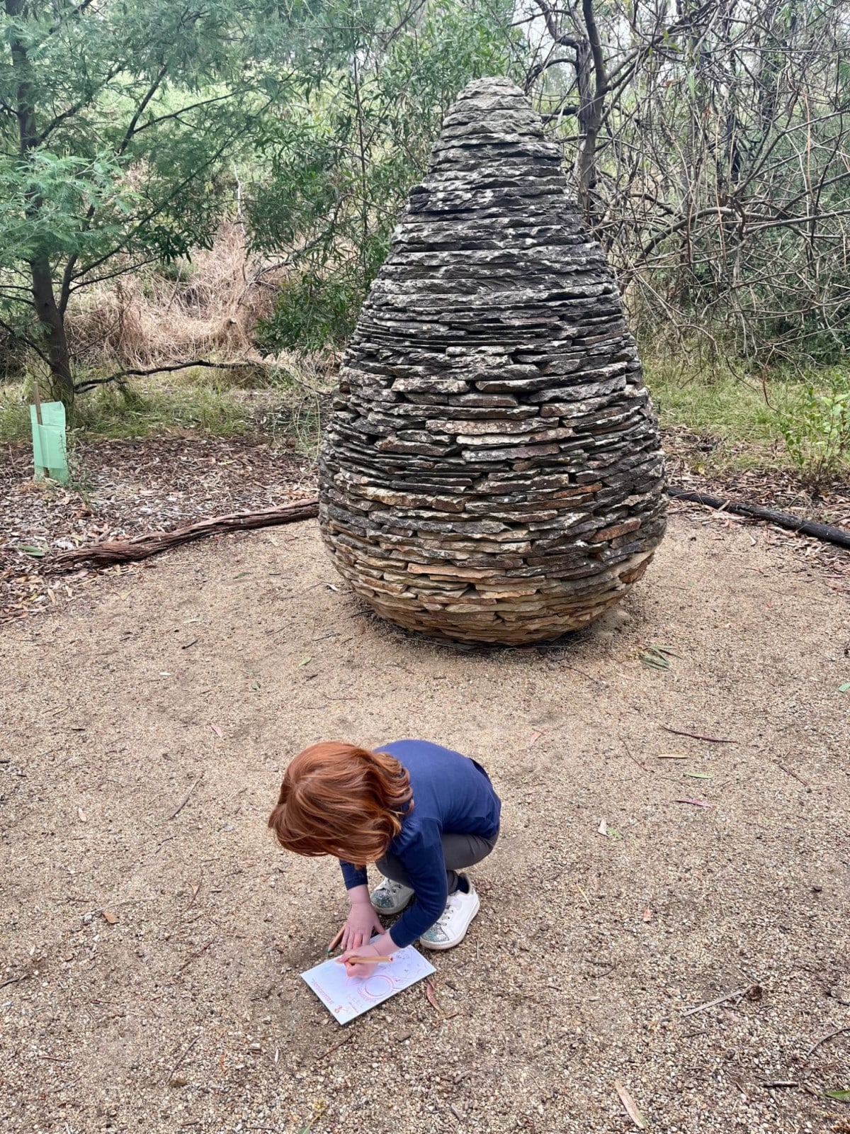 Girl drawing in journal card next to sculpture