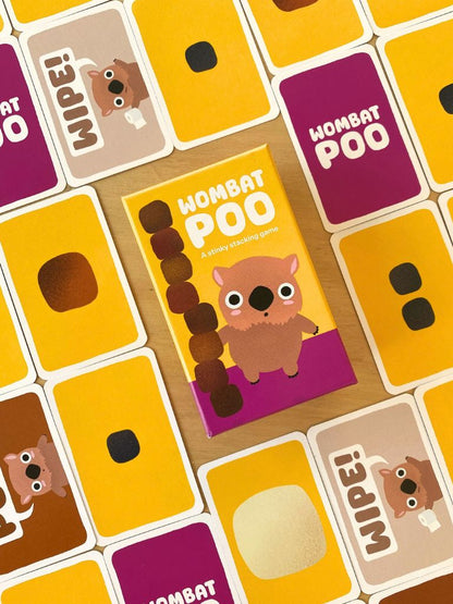A colorful children's card game titled 'WOMBAT POO' arranged on a wooden surface, with multiple illustrated cards visible around it.